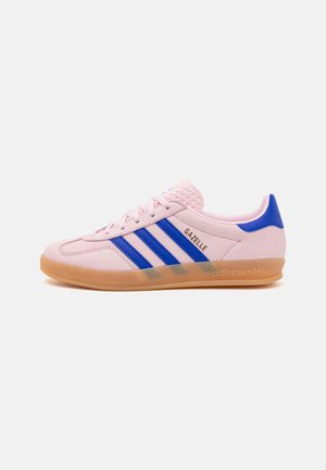 Niedriger Adidas Gazelle Sneaker, hellrosa mit blauen Streifen und Fersenlasche, Gummisohle und goldenem "GAZELLE"-Text an der Seite.