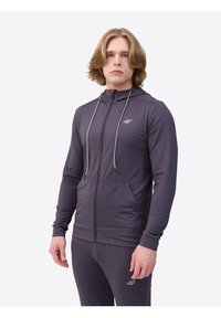 Herren Hoodie in Dunkelgrau, mit Reißverschluss vorne, zwei Seitentaschen und hellgrauen Kordeln. Hergestellt aus einem strukturierten, feuchtigkeitsableitenden Stoff.