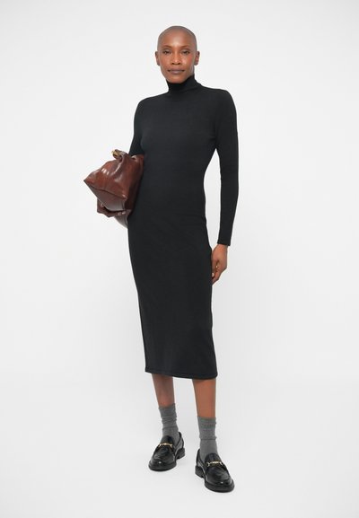 Melnā garo piedurkņu kleita ar augstu kaklu, pieguļošs siluets, gluda tekstūra. Pievienota brūna ādas soma un pelēkas zeķes.