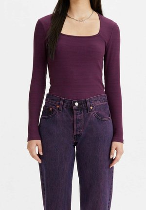 Femme portant un haut ajusté à manches longues côtelées avec un col carré et un jean en denim violet foncé taille haute.