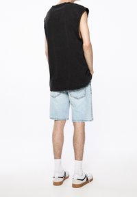 Mustia läskitön toppi, vaaleansiniset farkkushortsit, valkoiset sukat ja rentommat kengät. Keskittyminen rentoon istuvuuteen ja yksinkertaiseen, siistiin muotoiluun.