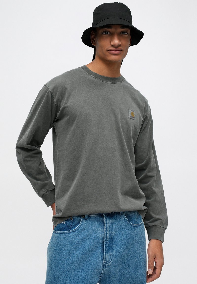 Olijfgroen, lang mouwen t-shirt van katoen, met een logopatch op de borst. Gepaard met lichtblauwe, high-waisted spijkerbroek.