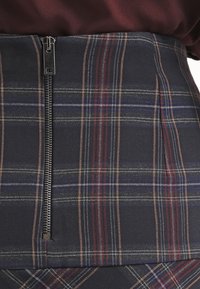 Hög midjefodrad rutad kjol med marinblå, röd och grön rand; har en framfickslåsningsdragkedja och ett strukturerat tyg med vecken.