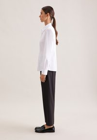 White button-up shirt with long sleeves, paired with black tailored trousers and black loafers. Plain design, smooth fabric, minimalist style.