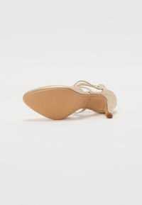 Pantof beige cu toc înalt, cu un toc subțire, cu un superior din piele netedă și un design cu vârf deschis. Talpa are o finisare texturată.