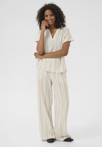 Ensemble de loungewear rayé beige comprenant un haut à manches courtes en V et un pantalon large avec poches latérales. Tissu doux avec une coupe décontractée.