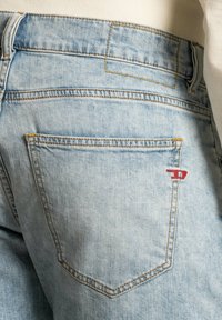 Jeans in denim blu chiaro con una texture sbiadita, dotati di un logo ricamato rosso sopra la tasca destra e cuciture gialle a contrasto.