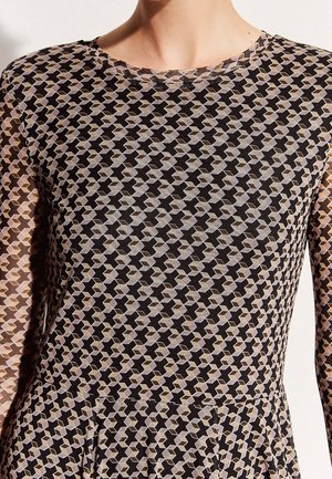 Donna che indossa un vestito a maniche lunghe con un motivo geometrico di forme intrecciate nere, beige e viola chiaro.