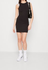 Svart figurnära klänning med rund halsringning, prydd med vita remmar. Kombinerad med vita platåsneakers och en svart handväska.