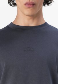 Czarnoszary t-shirt z okrągłym dekoltem, wykonany z gładkiej tkaniny, z subtelnym wytłoczonym logo na klatce piersiowej. Klasyczny krój, minimalistyczny design.