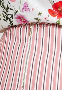 Hedvábný top s květinovým potiskem má krátké rukávy a kulatý výstřih. Dole je růžová pruhovaná sukně s viditelným zipem a tenkými černými akcenty.