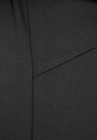 Un tissu noir au toucher lisse présente un design de couture angulaire, créant une apparence moderne et structurée.