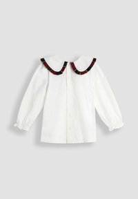 Blusa bianca a maniche lunghe con bottoni frontali e un ampio colletto rotondo rifinito con tessuto arricciato rosso e nero.