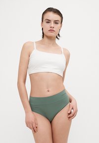 Biely crop top s tenkými ramienkami a vysoko pásovými, olivovo zelenými nohavičkami z hladkej, elastickej tkaniny. Minimalistický dizajn bez viditeľných vzorov.
