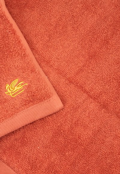 Serviette orange texturée avec un petit détail de fleur jaune brodée dans le coin plié.