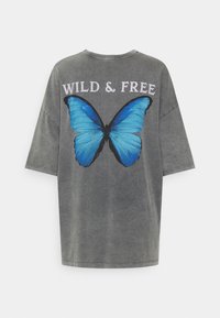 Šedé oversize tričko s krátkým rukávem, na zadní straně se nachází velká modrá motýl a text "WILD & FREE".