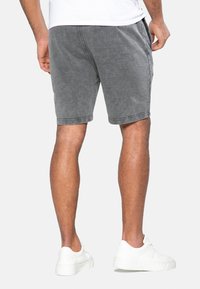 Shorts en coton gris avec un délavage, ceinture élastique et poches sur les côtés. Portés avec des baskets blanches, montrant un style décontracté.