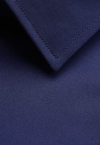Navy blue fabric with a fine, textured weave. The image features a folded collar with neat stitching along the edge.