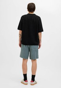 Cămașă tricotată neagră cu mâneci scurte și model cu țesătură deschisă, asortată cu pantaloni scurți din corduroy bleu deschis și încălțăminte casual cu accente roșii.