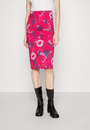 Femme portant une jupe crayon rouge à imprimé floral large rose et violet, un haut blanc sans manches et des bottes noires à talons mi-mollet.