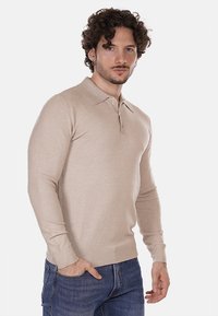 Polo a maniche lunghe beige con colletto, patta con bottoni e polsini a costine, realizzato in tessuto morbido, abbinato a jeans in denim blu.