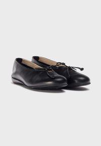 Zapatos planos de cuero negro con punta redondeada y un pequeño lazo en la parte frontal. Superficie suave con una suela flexible para mayor comodidad.
