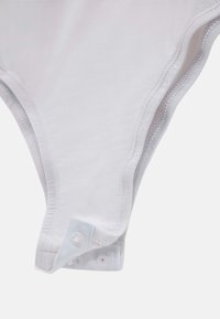 Body en coton blanc avec des fermetures à pression en bas, présentant un tissu doux, une texture lisse et des coutures le long des bords.