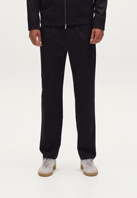 Pantalones oscuros fabricados en tejido suave, con un corte recto. Combinados con zapatillas de color claro. Diseño simple y moderno.