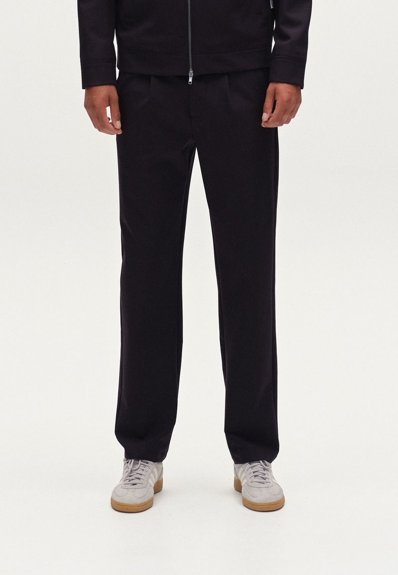 Pantalones oscuros fabricados en tejido suave, con un corte recto. Combinados con zapatillas de color claro. Diseño simple y moderno.