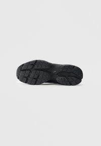 Black rubber shoe sole with deep grooves and textured tread pattern for grip, displayed on a plain white background.