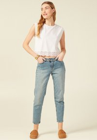 Witte cropped top met kantafwerking, gedragen met lichtblauwe rechtlopende jeans en bruine instappers. Eenvoudig, casual ontwerp zonder patronen.