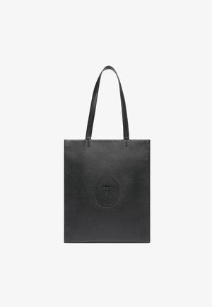 Bolso tote de cuero negro con dos asas largas, forma cuadrada, textura suave y un logo circular en relieve en el frente.