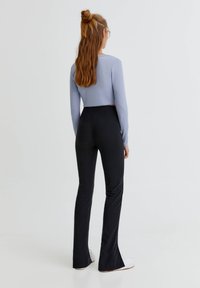 Top corto de manga larga azul claro combinado con pantalones acampanados negros de cintura alta. La tela parece suave, con una textura lisa y un brillo sutil.