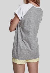 Camisa corta de manga corta en gris y blanco con un corte relajado, que presenta un escote redondo y una textura suave, combinada con pantalones cortos amarillos.