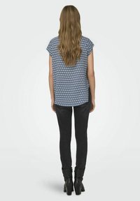 Mornarska kratka bluzica s potiskom in geometrijskimi vzorci, združena z oprijetimi črnimi jeans hlačami in gležnjarji. Zadašnji pogled, dolgi lasje so vidni.