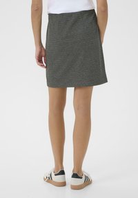 Grijze rok met een textuurpatroon, tot halverwege de dijen, en een rechte snit. Gecombineerd met witte sneakers met zwarte accenten en een gumrubberen zool.