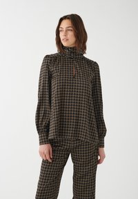 Mustmustritsiga must blouse, millel on kõrge kaelus, võtmeaugu detail ja pika varrukaga kokku tõmmatud mansetid, valmistatud siledast kangast.