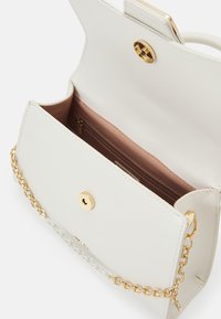 Sac à main en cuir blanc avec des accessoires en or. Il dispose d'une chaîne en bandoulière, d'une fermeture à pression et d'un intérieur rose pâle avec une poche zippée.