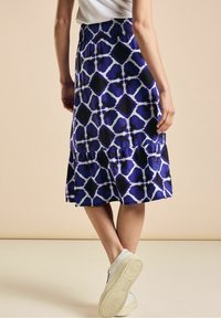 Sininen ja musta kuvioitu midihame, jossa on smokkivyötärö, kerroksittainen malli ja kevyt kangas. Stailattu valkoisilla tennareilla.