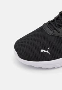 Scarpa da ginnastica nera con tomaia in rete, suola bianca e dettaglio del logo. Punta tonda e design curvato con sistema di allacciatura per una vestibilità sicura.