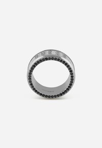 Zilverkleurige ring met een gestructureerde band, zwarte edelstenen rondom de rand en reliëfdetails op het bovenoppervlak.