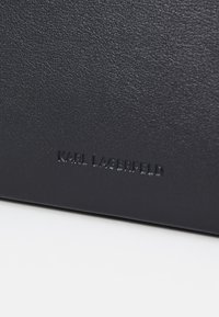 Černá texturovaná kůže s embosovaným logem "KARL LAGERFELD". Hladký povrch dodává hloubku; minimalistický design s jemnými detaily.