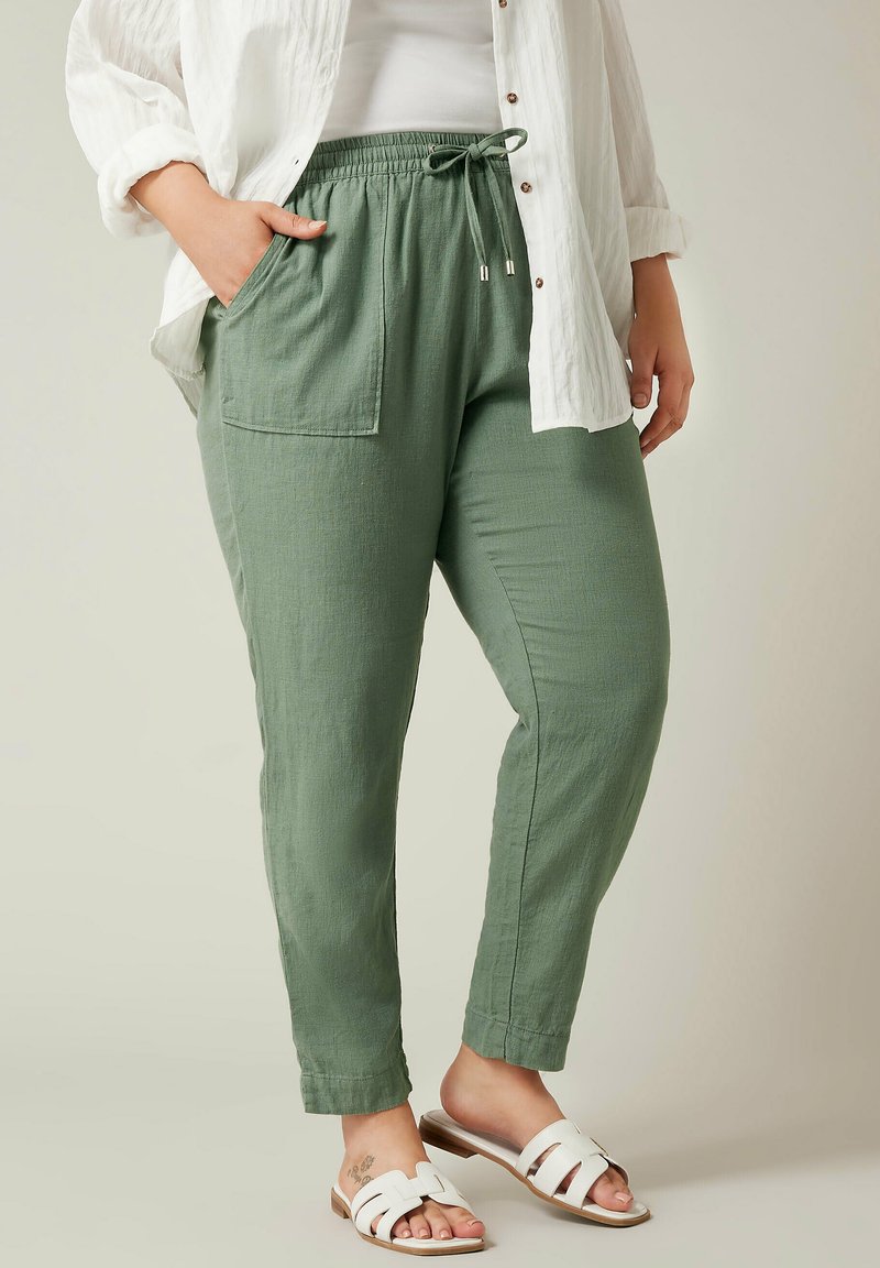 Lichtgroene, linnenmix broeken met een elastische tailleband, trekkoord en zak, gestyled met een witte, geknoopte blouse en witte sandalen.