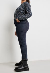 Halenka s dlouhým rukávem v námořnické modři se světle hnědými vzory, spárovaná s tmavými džíny skinny a černými kotníkovými botami s masivní podrážkou.