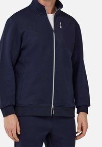 Navy blue zip-up jacket with high collar, zippered front, and side pockets. Features a smooth texture and ribbed cuffs and hem.