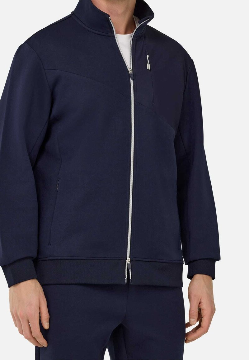 Navy blue zip-up jacket with high collar, zippered front, and side pockets. Features a smooth texture and ribbed cuffs and hem.