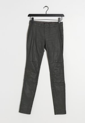 Pantalon slim en simili cuir noir suspendu à un cintre noir sur un fond blanc, avec des panneaux cousus aux genoux.