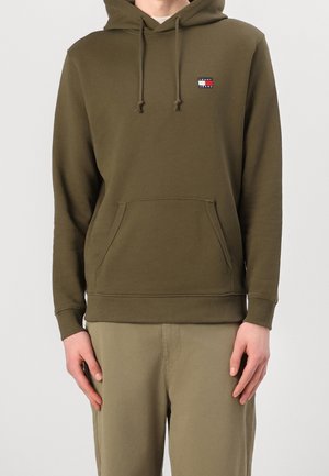 Bluza z kapturem w oliwkowej zieleni, wykonana z miękkiego materiału, z kieszenią typu kangur, ściągaczami na mankietach oraz naszywką z logo Tommy Jeans na lewej piersi.