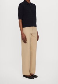 Polo a maniche corte blu navy con motivo testurizzato, abbinata a pantaloni beige a gamba larga. Scarpe basse nere completano il look.