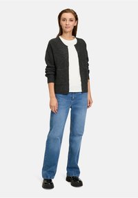 Ciemnoszary kardigan o miękkiej fakturze i okrągłym dekolcie, noszony na białej koszuli, w połączeniu z niebieskimi dżinsami i czarnymi butami na platformie.